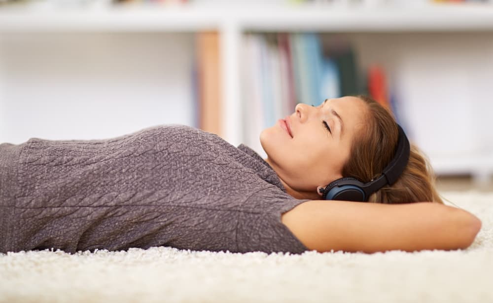 A young woman practicing guided meditation with headphones on, sitting calmly with closed eyes.