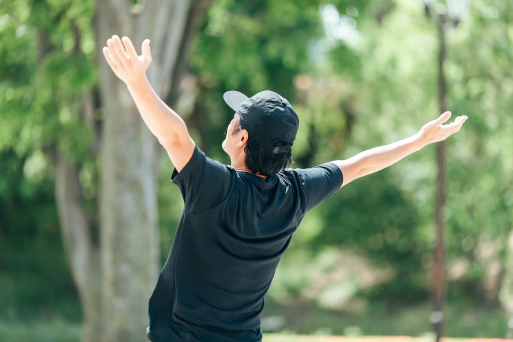 A person practicing forest bathing while through a peaceful green forest.