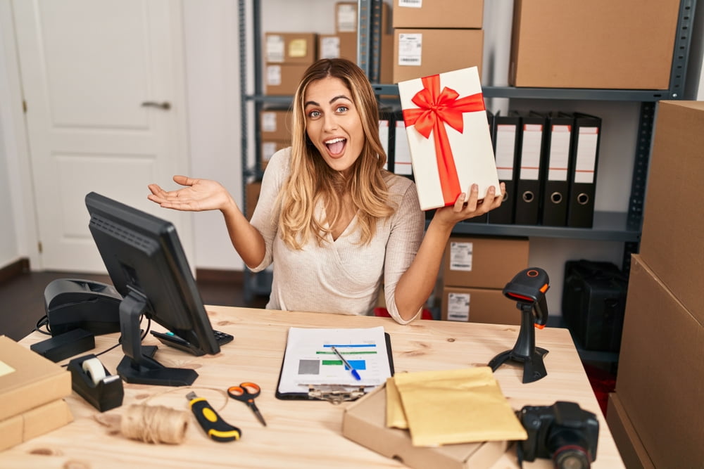 Happy female entrepreneur celebrating a small achievement while holding a wrapped gift box at her desk