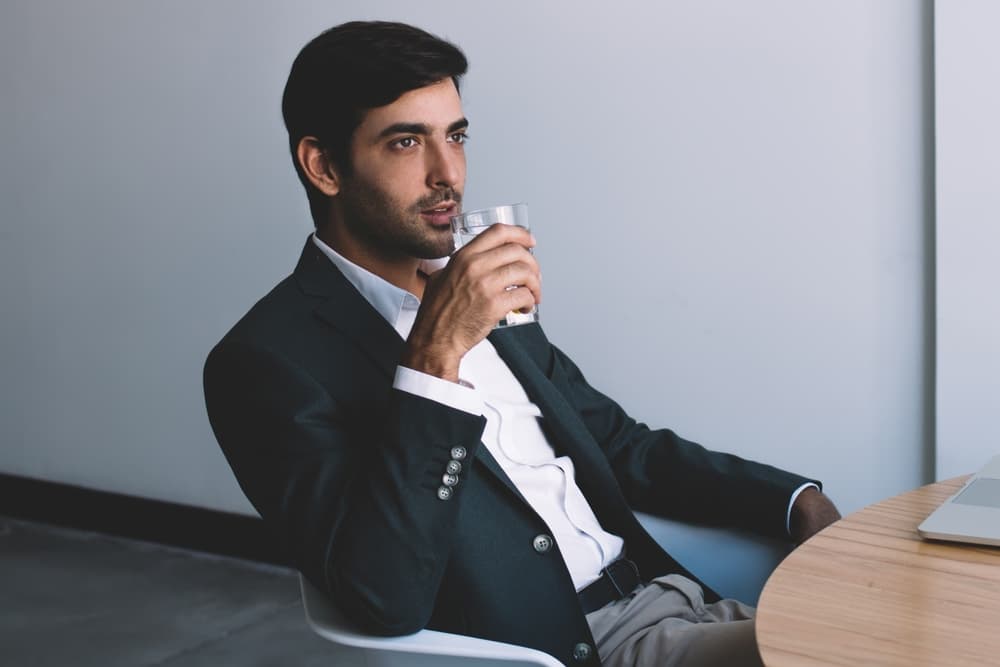 Business professional sitting at office desk drinking a glass of water during a work break
